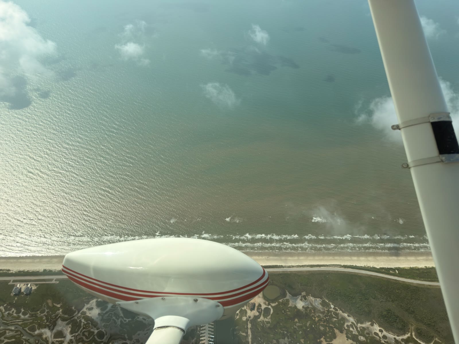View from a Cessna 172 wing over the Gulf Coast near Pearland, Texas, with scattered clouds and sunlight reflecting on the water.